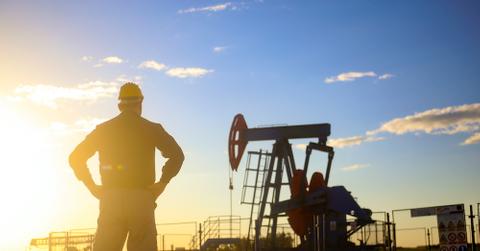 A man standing by an oil pumpjack.