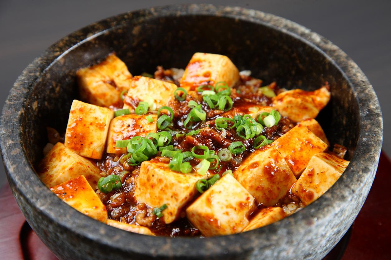 Cooked tofu covered in a sauce and topped with green onions in a bowl