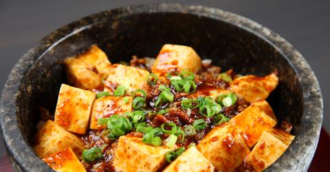 Cooked tofu covered in a sauce and topped with green onions in a bowl
