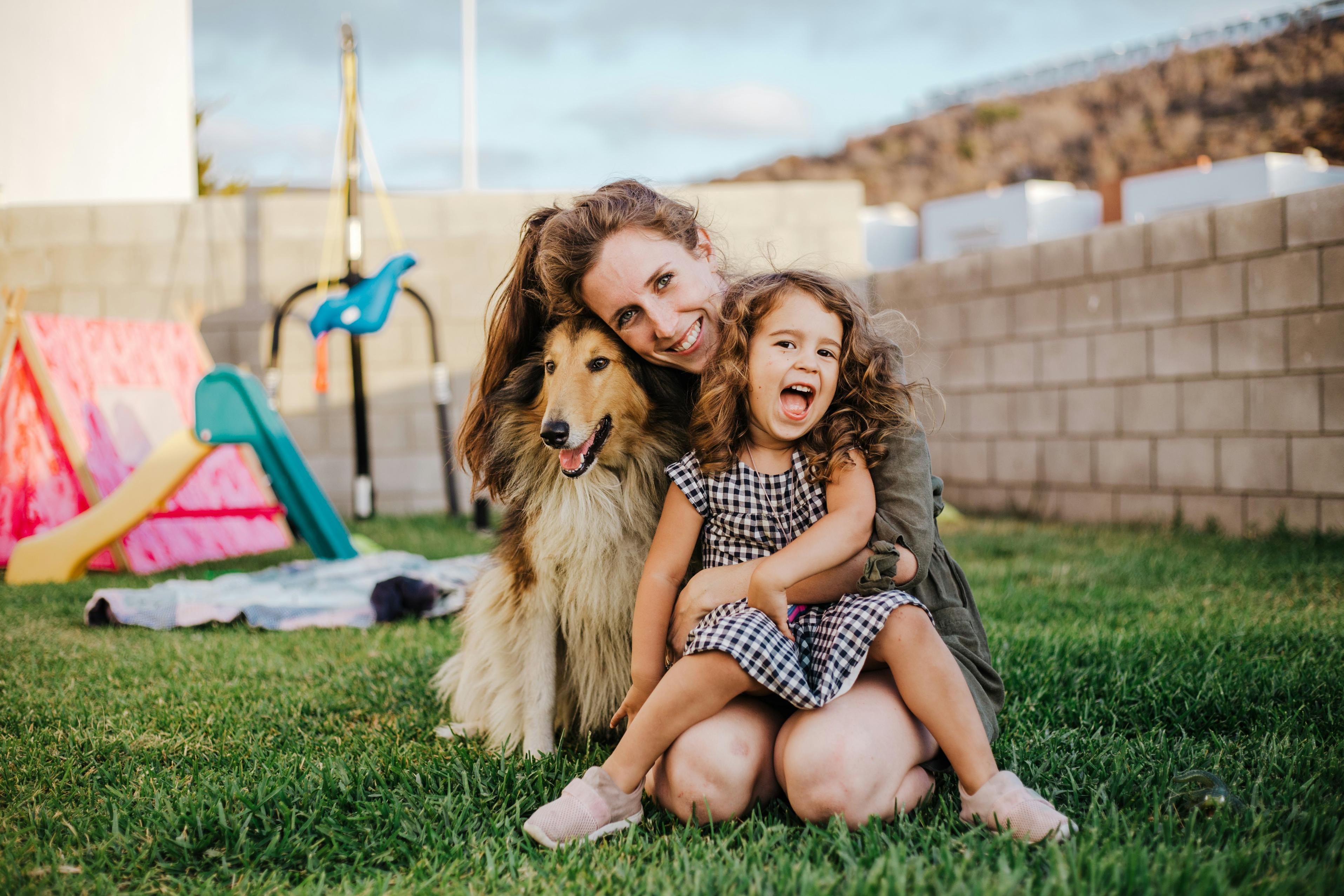 A smiling mom and daughter pose in the backyard with their companion dog.