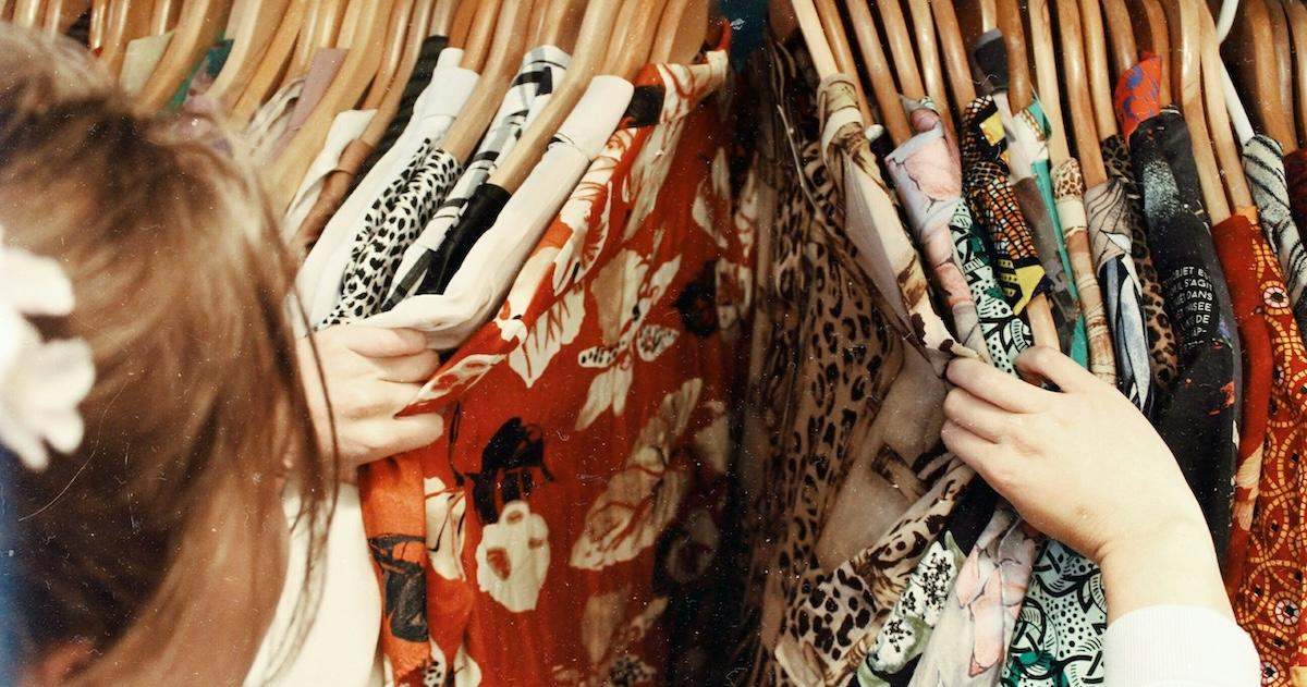 Person browsing various patterned shirts on rack in secondhand store.