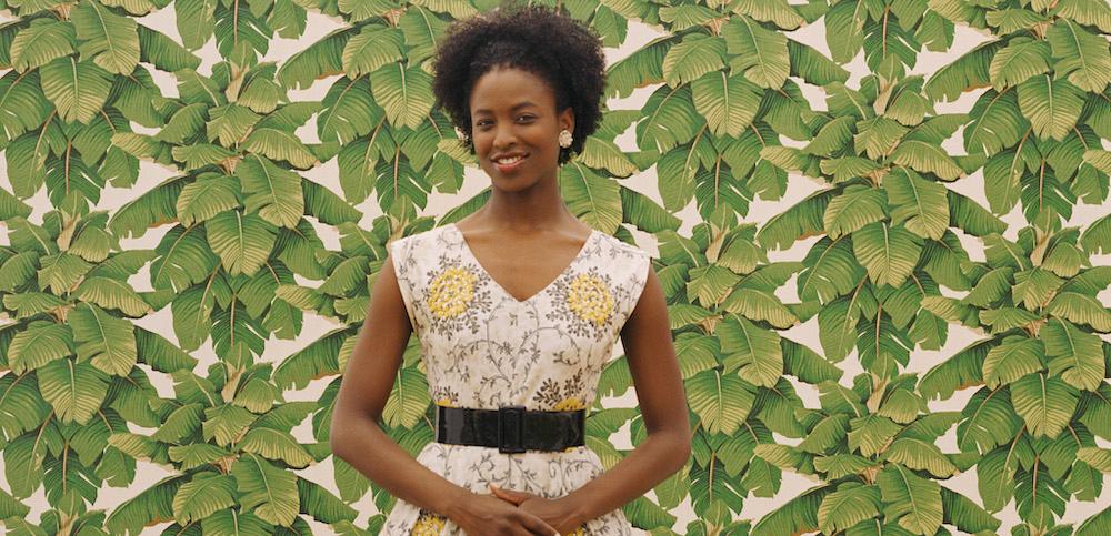 A woman standing in front of leafy wallpaper.