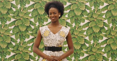 A woman standing in front of leafy wallpaper.