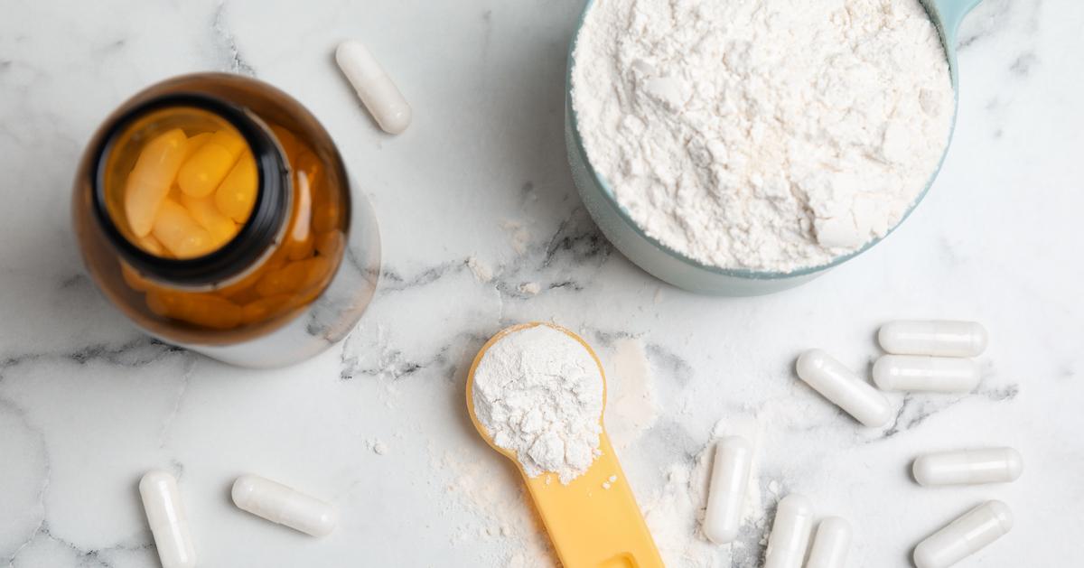 Powdered creatine supplements in a measuring cup and measuring spoon, and a jar of capsules