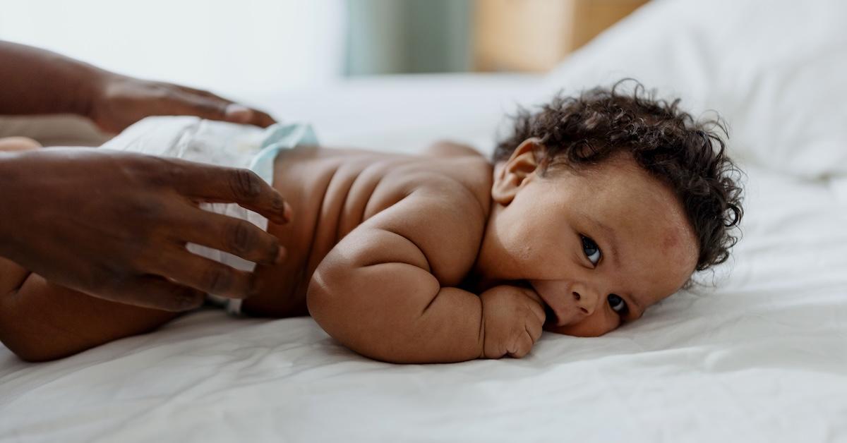 Baby boy in diaper on bed with parent