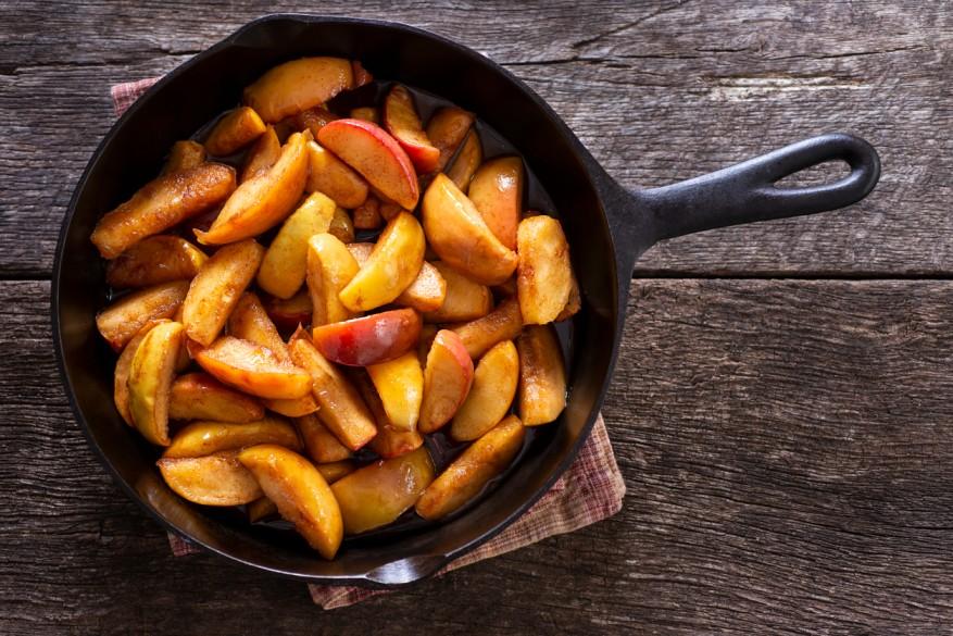 A skillet is pictured with caramelized cinnamon apples atop a wooden table.