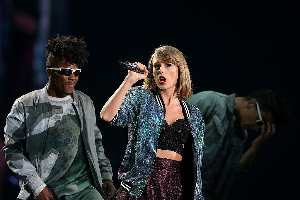 Taylor Swift wearing a blue sparkly jacket over a cropped black sparkly tank top on her "1989" world tour