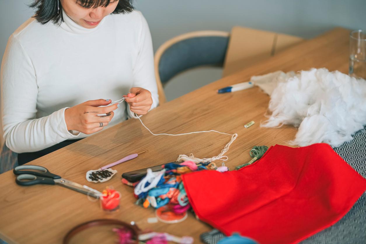 Someone sitting at a table holding white thread between their fingers.