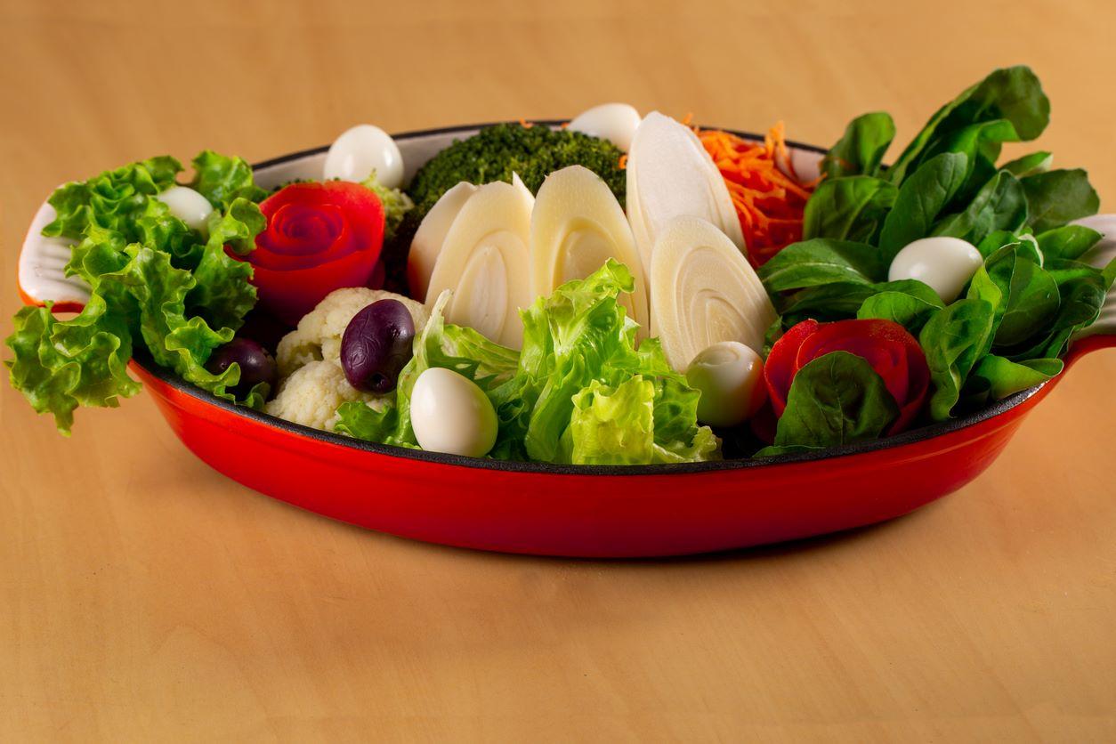 In a red baking tray, a salad featuring hearts of palm, olives, and more