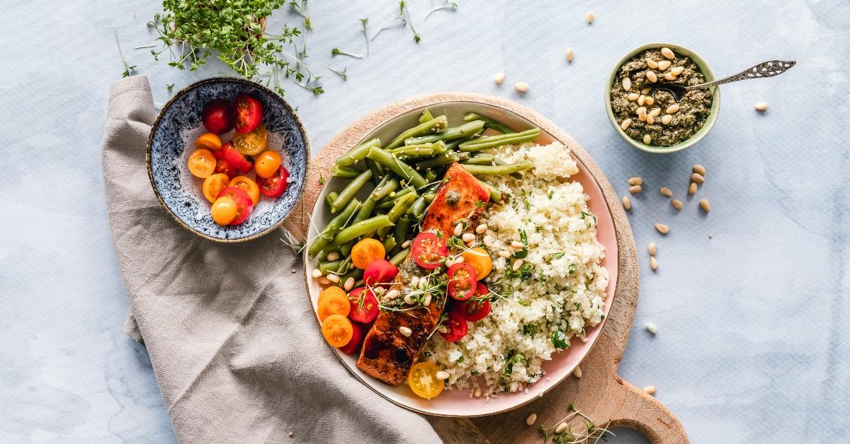 A meal of a piece of salmon, green beans, rice, and cherry tomatoes presented on a clay dish.