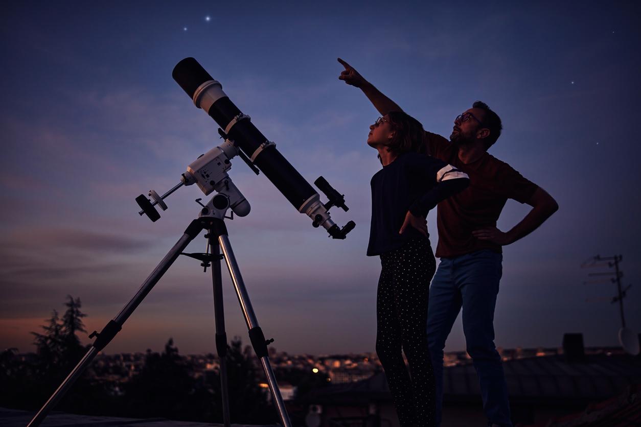 A father and daughter observe and point up towards the night sky beside a telescope.