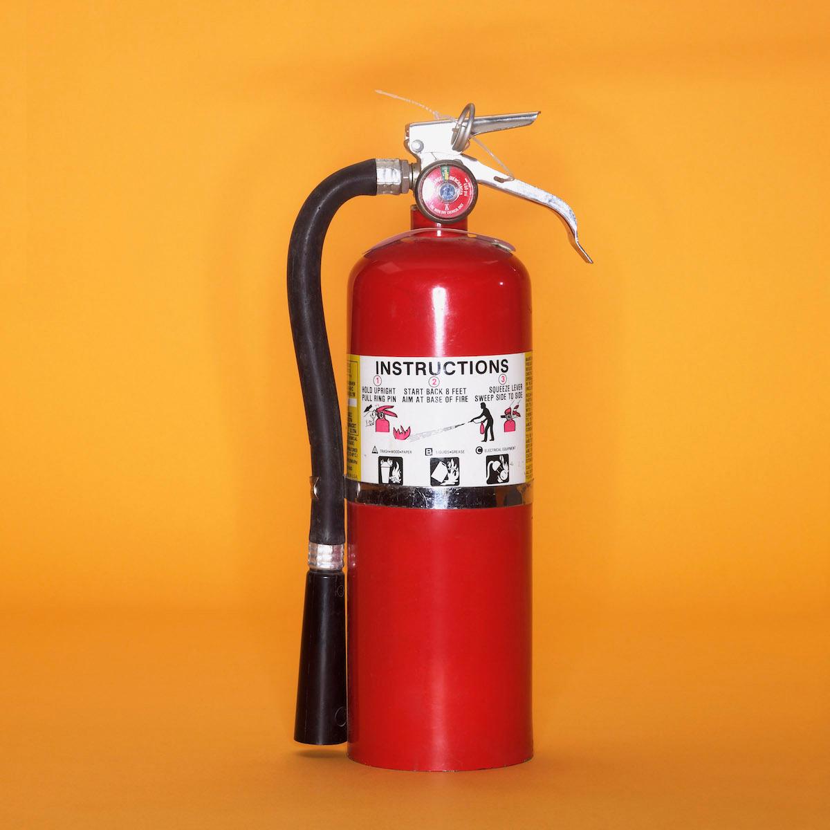 A fire extinguisher standing against an orange background. 