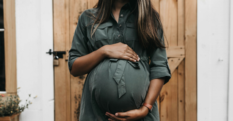 A pregnant person holds their belly while standing against a door
