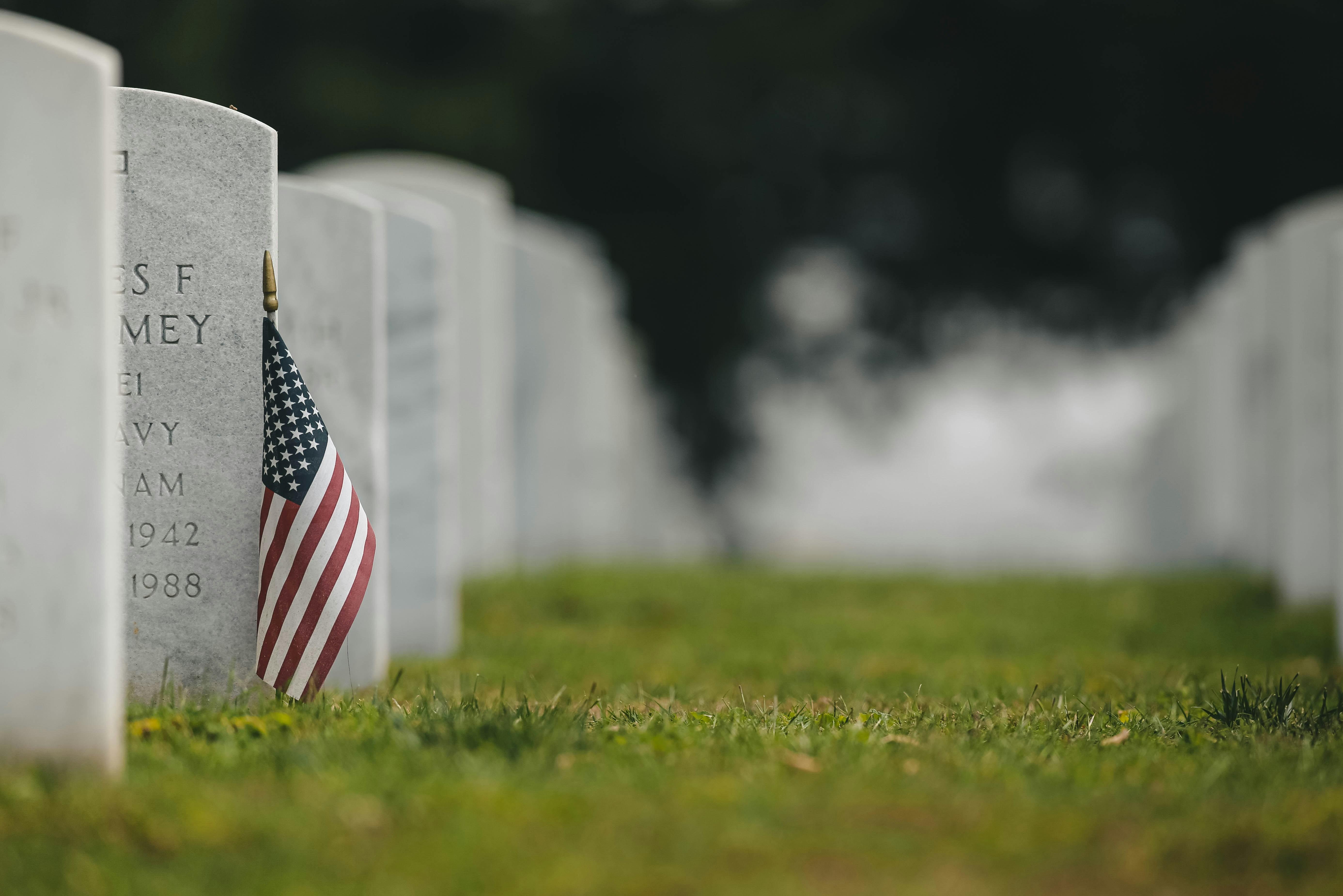 An American flag is pictured beside a headstone in a cemetary.