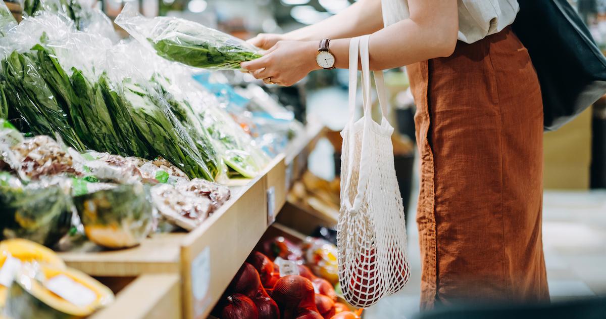 Someone with a mesh shopping bag shops for greens in the supermarket