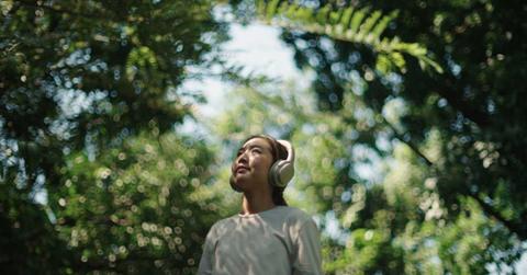 A woman wears headphones while relaxing in nature (Representative Cover Image Source: Getty Images | pocketlight)