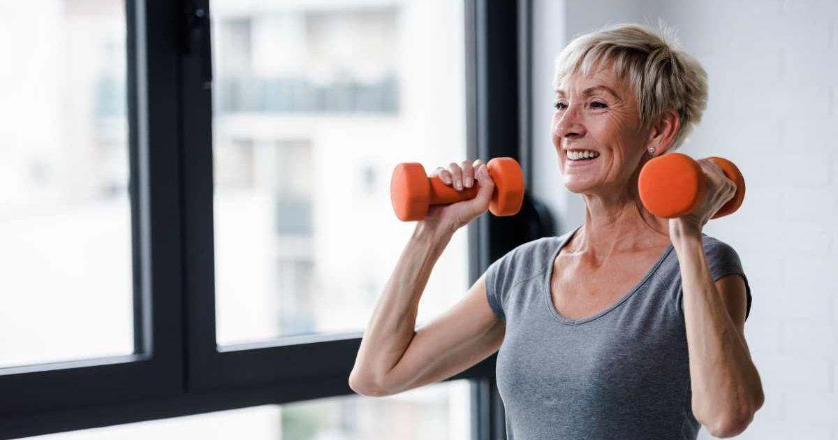 Elderly woman smiling while holding dumbells at home during workout. (Representative Cover Image Source: Getty Images | Lordn)