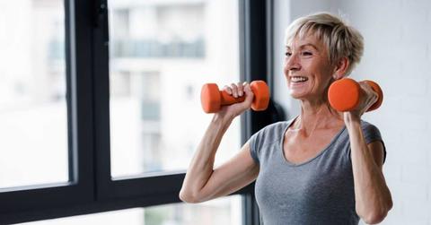 Elderly woman smiling while holding dumbells at home during workout. (Representative Cover Image Source: Getty Images | Lordn)