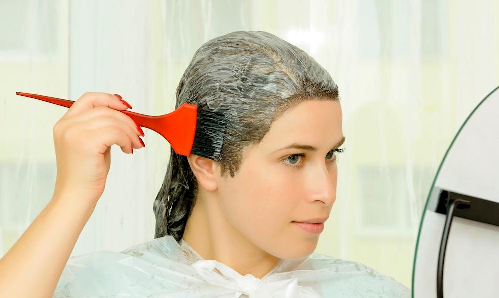 A person using a brush to apply product to their hair in a mirror. 