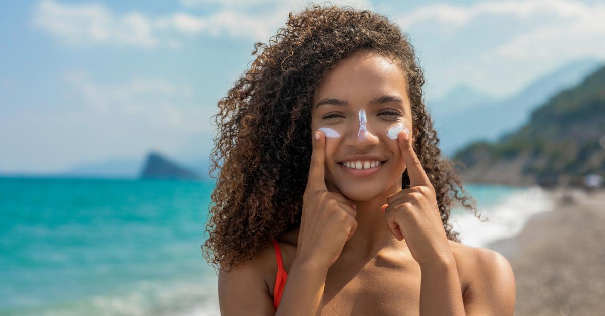 Close-up photo of woman on a beach pointing to sunscreen on her face