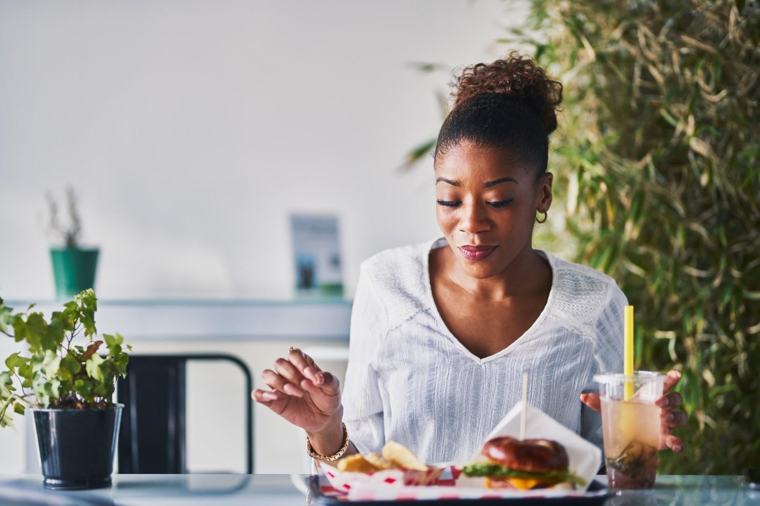 A woman sits down to enjoy a healthy vegan lunch with a drink in hand and a plant by her side.