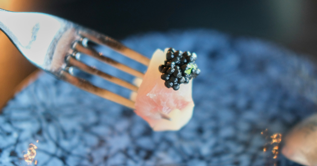 A fork holds a piece of meat topped with black caviar