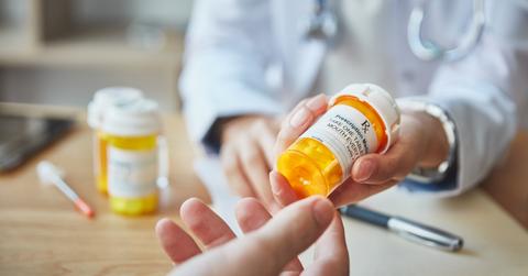 A pharmacist in a white coat hands a prescription pill bottle to a customer.