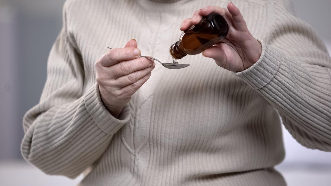 Person pouring liquid supplement into a spoon.