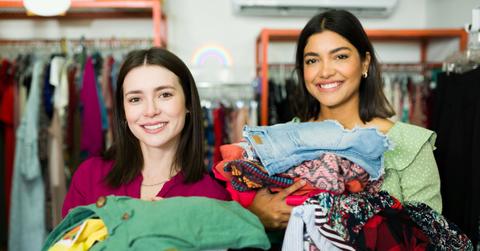 Two women in a thrift store, holding piles of of clothing