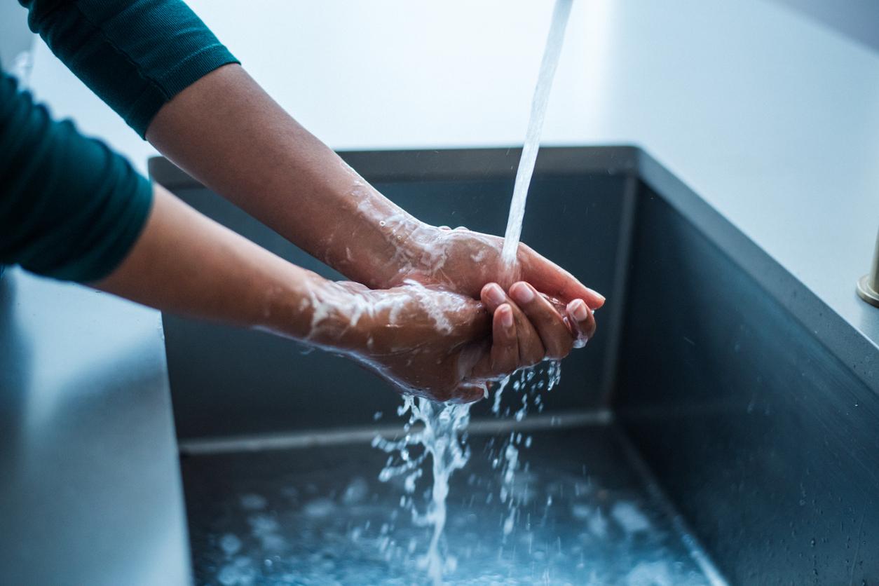 A person wearing long sleeves washes their hands with soap and water in a deep black sink.