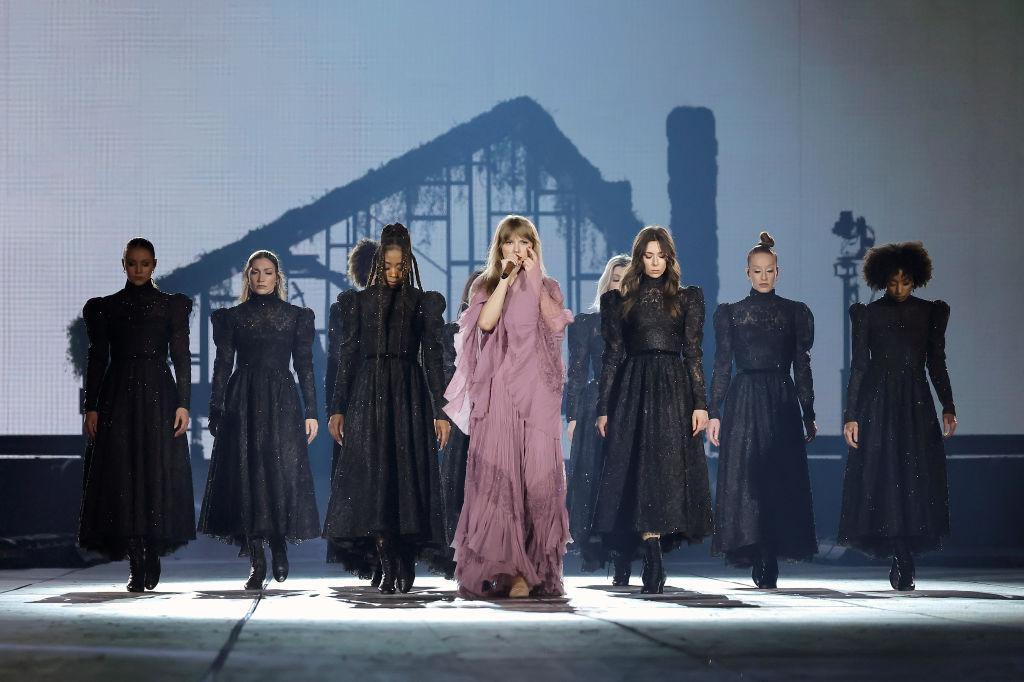 Taylor Swift performing on opening night of the Eras Tour in a pink dress, surrounded by backup dancers wearing black