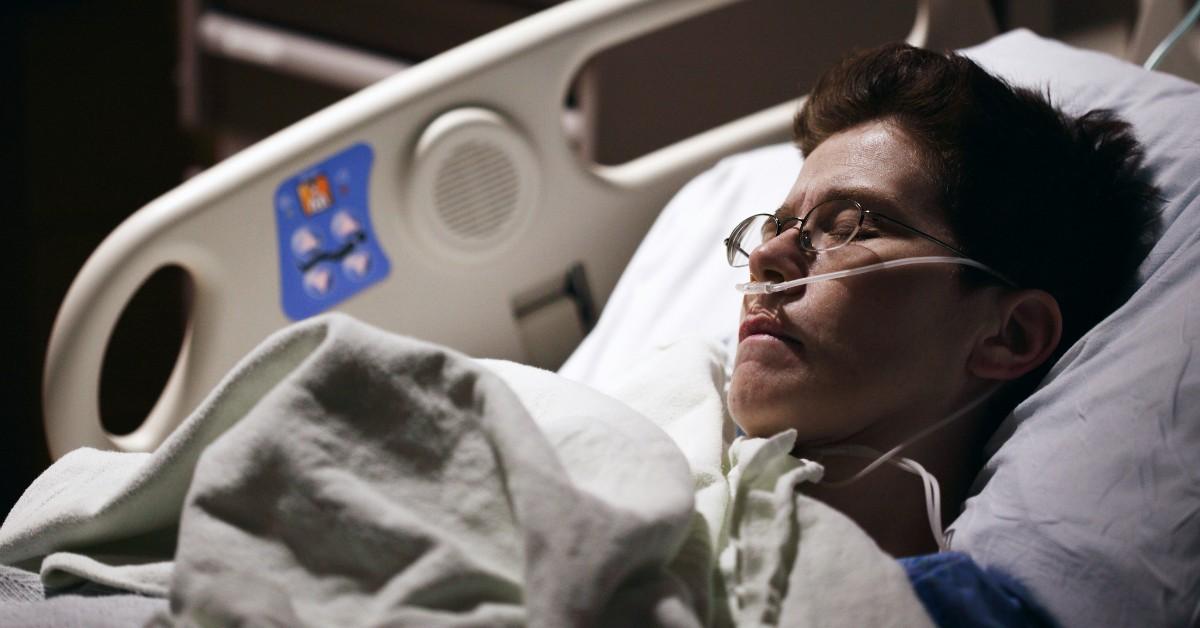 A man lies in a hospital bed with his eyes closed