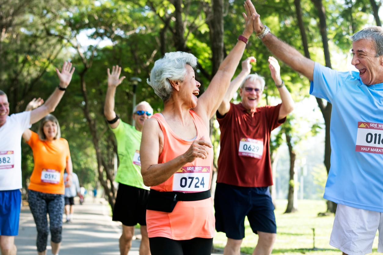 A group of older adult runners celebrate as they cross the finish line of a marathon.