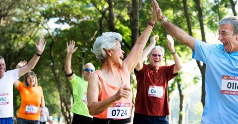 A group of older adult runners celebrate as they cross the finish line of a marathon.