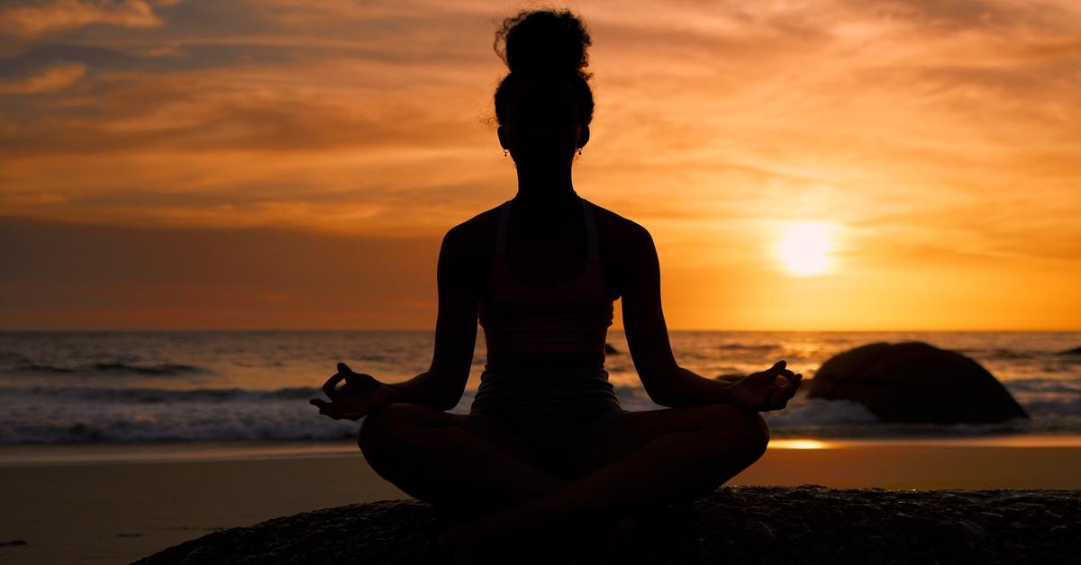 Woman meditating on a beach as the sun sets. 