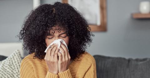 A woman sitting on a couch blowing her nose into a tissue.