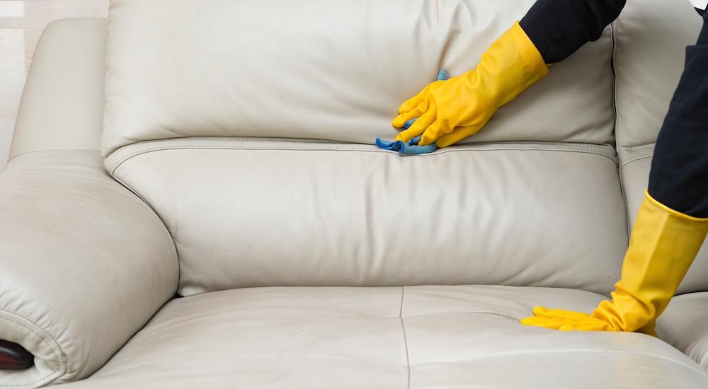 Someone is wearing gloves to clean a white leather couch. 