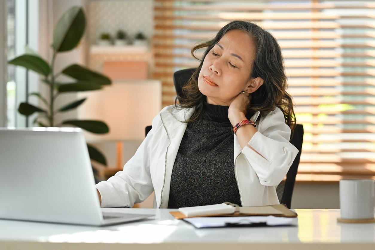 A woman in a white coat sits at her desk and cracks her neck.