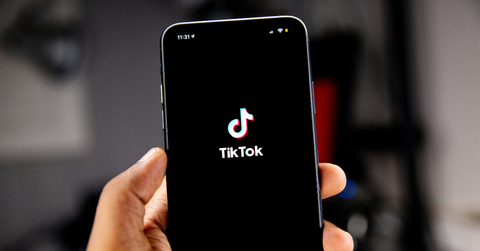 A person holds their phone up with the TikTok logo showing