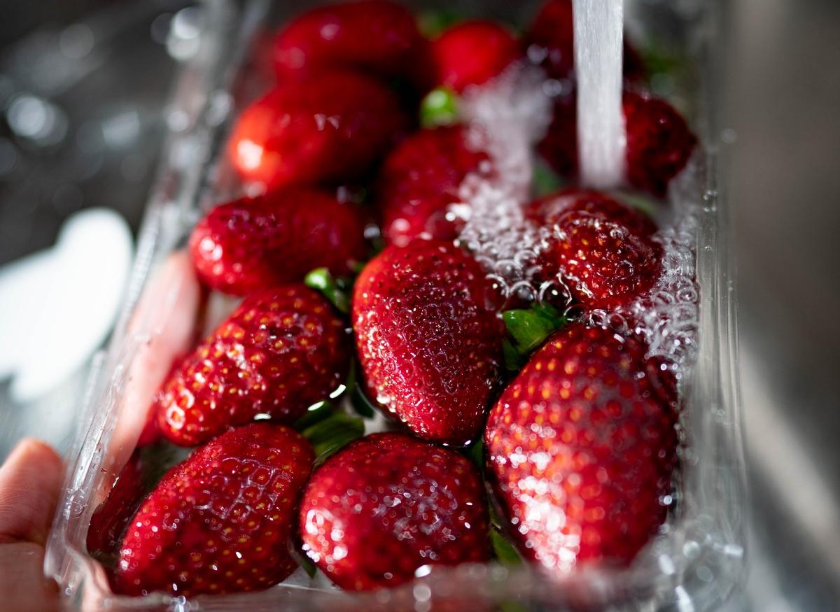 running water over package of strawberries