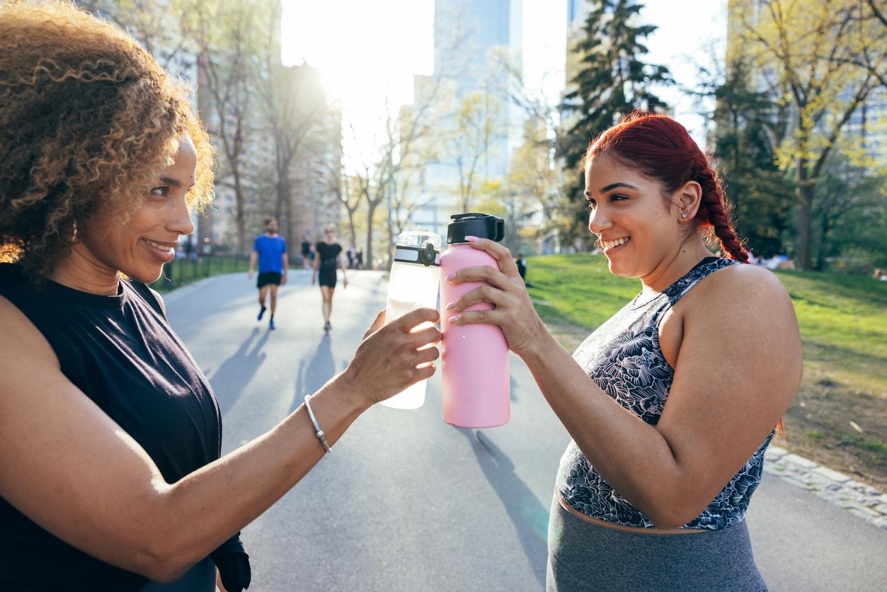 Two smiling friends display their reusable water bottles during a walk in Central Park in New York City.