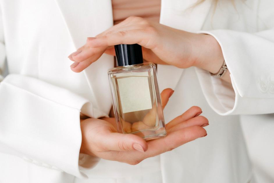 Close up photo of the hands of a woman wearing a white coat holding a brandless bottle of perfume. 