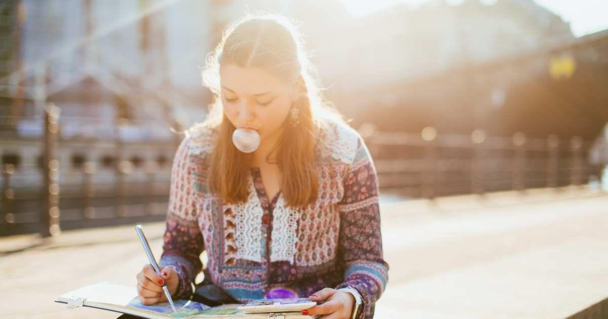A woman is painting while sitting on the street while popping bubbles with her chewing gum. (Representative Cover Image Source: Getty Images | Guido Mieth)