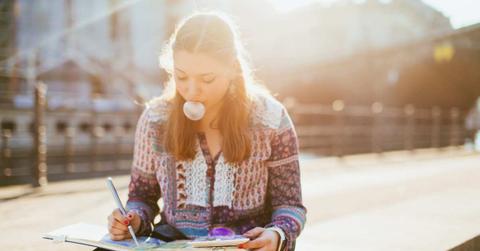 A woman is painting while sitting on the street while popping bubbles with her chewing gum. (Representative Cover Image Source: Getty Images | Guido Mieth)
