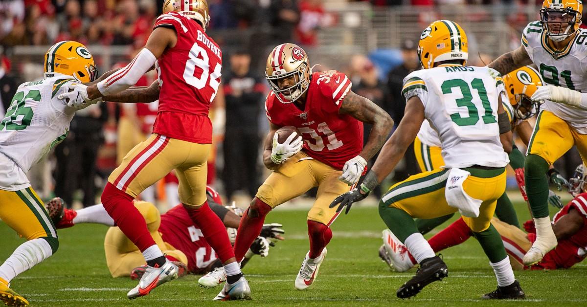 A 49ers player runs between the other team while carrying a football 