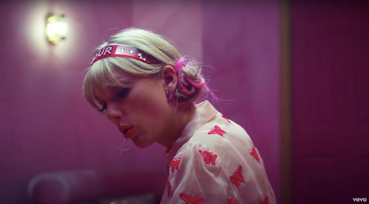 Taylor Swift wearing a pink head band and a light pink shirt with butterflies on it in her "Lover" music video