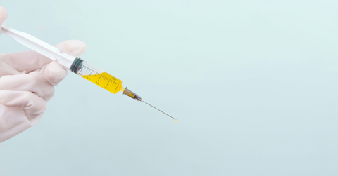 A gloved hand holds a syringe of yellow liquid