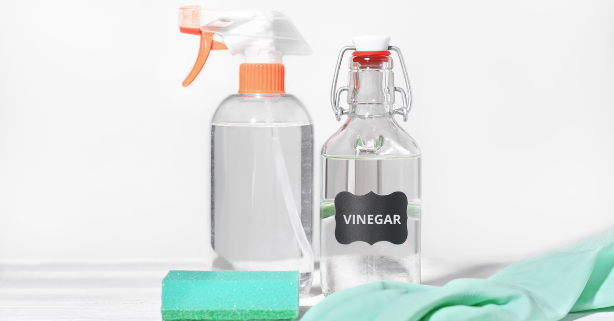 A bottle of cleaning vinegar sits next to a spray bottle, sponge, and dish gloves