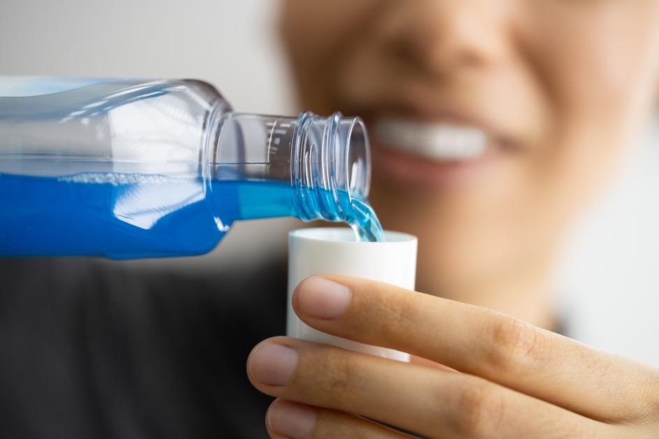 A person pours blue mouthwash into a cap.