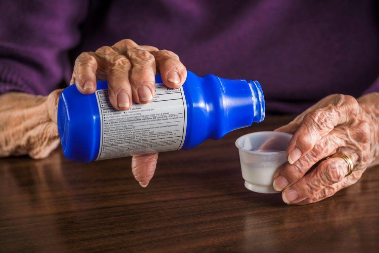 Senior lady's hands holding a medicine bottle with small cup